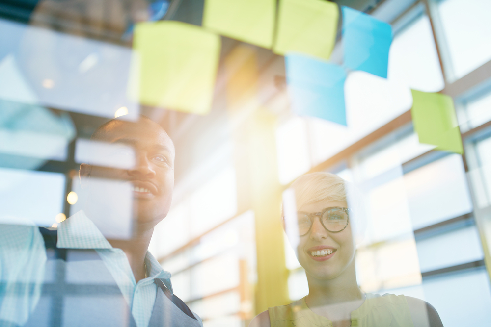 Two creative millenial small business owners working on social media strategy brainstorming using adhesive notes in windows